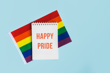 LGBT raibow flag ribbon with notebook or note mock up on light blue background. Flat lay, top view, trendy minimal composition, concept of gay pride of proud month lgbtq community. Cultural divesity