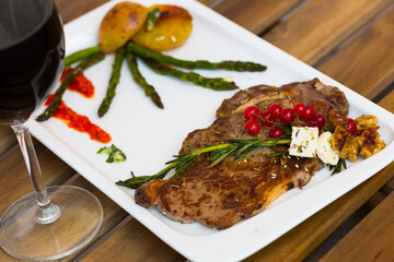 Appetizing grilled veal loin with baked vegetables served with redcurrant on ceramic plate on wooden background..