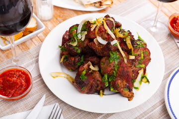 Pork shashlik with onion and greenery served on circular white plate with glasses of wine.