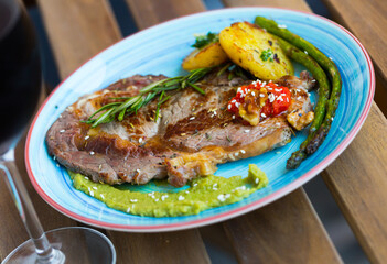Roasted veal steak with seasonings served with guacamole sauce and baked vegetables on wooden surface..
