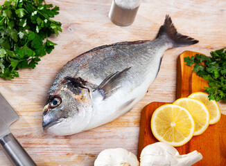 Fresh raw gilthead seabream with parsley, garlic, sliced lemon and spices on wooden kitchen table
