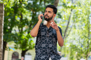 Hispanic man tourist having remote conversation communicate speaking by smartphone with friend, talking on phone unexpected good news gossip standing on urban city street. Town lifestyles outdoors.