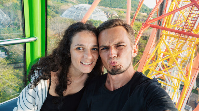 Selfie of happy couple tourists travelers in love in the cabin of a ferris wheel in amusement park on summer vacation