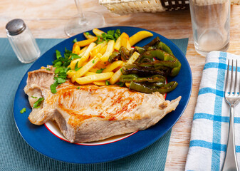 Close up of tasty baked pork with french fries and baked green pepper, served on plate