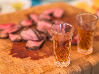 Cognac shots and sliced steak served on a wooden cutting board in a cozy indoor setting
