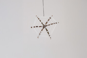 crafted spider web. using small sticks with string wrapped around them to form the web. Set against a plain grey background, Halloween decor and celebrations.