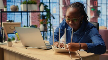 African american woman restarting her wireless router and checking network settings to resolve an...
