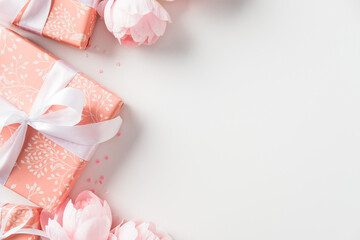 Pink gift boxes with white ribbons surrounded by peonies. Happy Mother's Day, birthday concept.