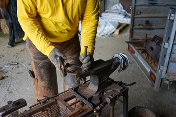 A person works on an anvil, with a hammer and a nail, to repair a horseshoe
