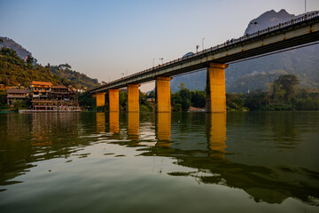 Concrete Bridge Over Nam Ou River at Sunset with Reflections and Riverside Village in Ngoy District, Laos