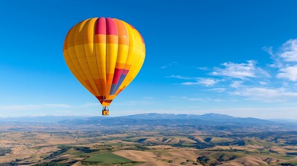 Obraz premium Hot Air Balloon Flying Over Colorful Landscape with Mountains Under a Blue Sky