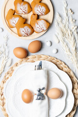 Festive Easter table setting with a white napkin and bunny decor. Gingerbread cookies and eggs add...