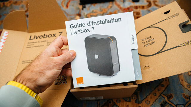 Paris, France - Feb 11, 2025: A person hand holds an installation guide for the new Orange Livebox 7 modem during an unboxing, showcasing the modem's packaging.