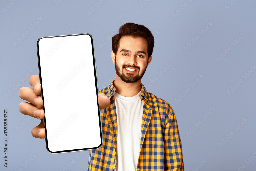 Poster Smiling Indian guy showing smartphone with mockup for mobile app design on screen, violet background