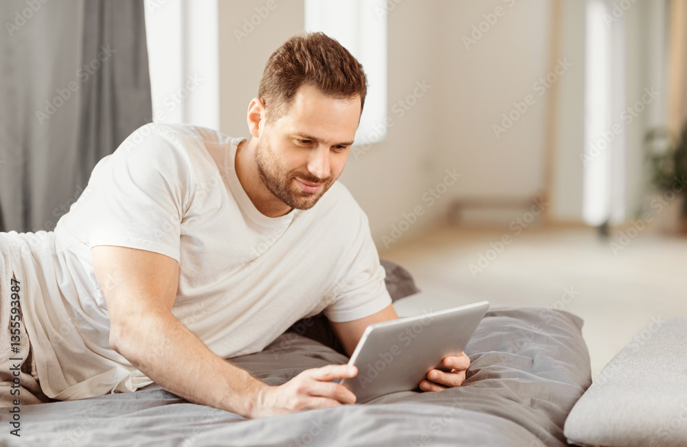 Aufkleber man in casual clothes using digital tablet lying in bed relaxing watching movie online in bedroom at