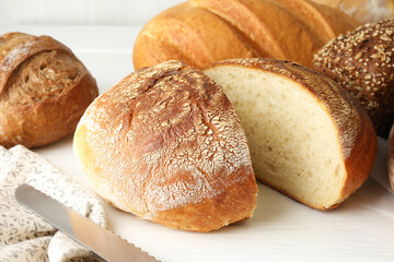 Cut loaf of freshly baked bread on white table, closeup