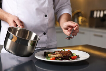Professional chef adding sauce to delicious dish at table indoors, closeup