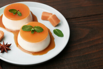Tasty puddings with caramel sauce served on wooden table, closeup. Space for text