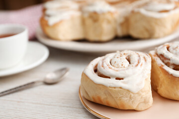 Delicious frosted cinnamon rolls on light wooden table, closeup