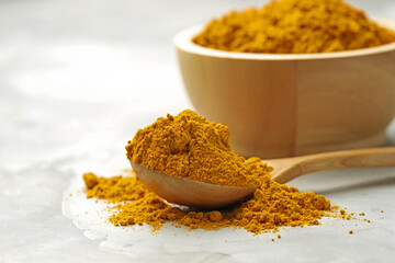 Turmeric powder and spoon on light grey table, closeup