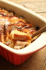 Taking tasty bread pudding from baking dish at wooden table, closeup