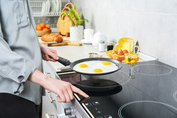 Woman cooking eggs in frying pan on cooktop indoors, closeup
