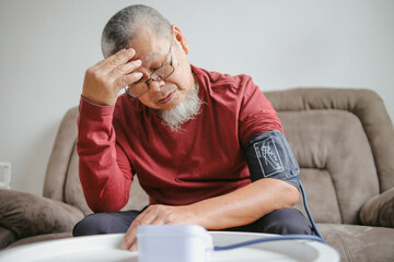 Fototapeta premium Senior Old Sick Male Suffering From Headache And Measuring Blood Pressure While Sitting on Sofa