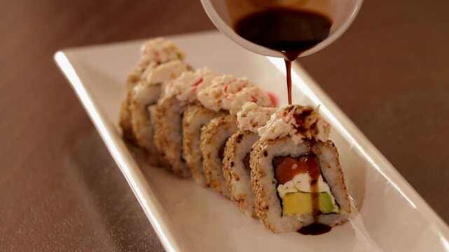 Rollo de sushi con tampico, cangrejo, queso crema y aguacate, sobre un plato blanco vertiendo salsa de soya en slow motion