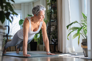 Happy smiling mature middle-aged woman with gray hair does plank exercise. Anti aging concept