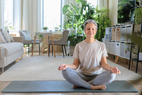 Smiling mature gray haired sport woman sits on yoga mat in lotus position. elderly lady meditates