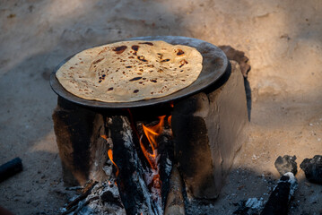 A village woman makes bread on the stove. cooking bread in clay stove , chula , makeing bread ,...