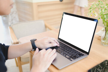 Person typing on a laptop with blank screen at a wooden table in a bright cafe, wearing a smartwatch.