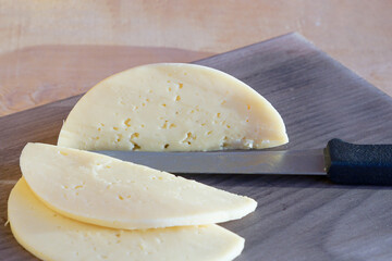 On the cutting board is cheese, slices of cheese and a knife.