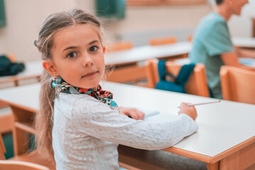 Happy school child girl during the class in the classroom looking at the camera.