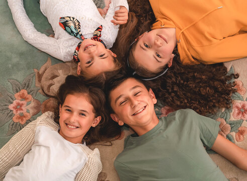 Happy group of children friends lying on the floor in a circle, looking at the camera, top view.