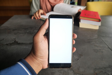 Hand holding a smartphone in a cozy study environment