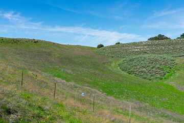 Rolling green hills with sparse vegetation are bordered by a wire fence and a not trespassing sign Santa Teresa County Park
