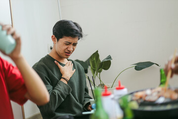Young Man In Green Sweater Holding Chest Showing Painful Feeling Chocked While Eating Food.