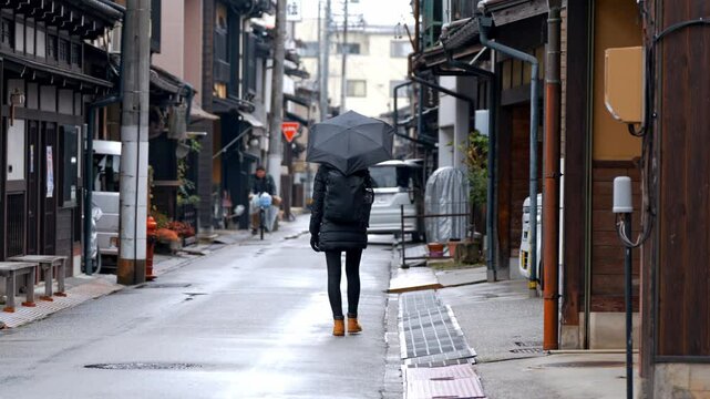 A woman strolls through the charming streets of Takayama on a rainy day, her umbrella shielding her from the gentle drizzle.