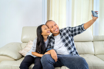 Obraz premium Happy father and daughter taking a selfie together on a couch at home