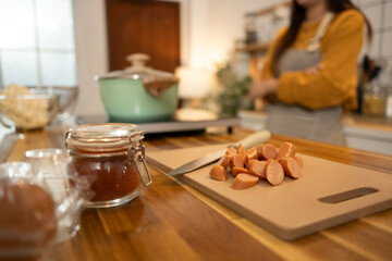 Close up of sliced sausages, sauce, and other ingredients on a wooden kitchen counter
