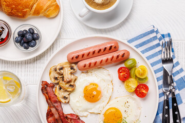 A classic breakfast plate featuring sunny-side-up eggs, crispy bacon, sausages, and fresh tomatoes