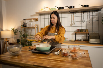 Young woman pouring cooking oil into a frying pan, ready to start the meal preparation