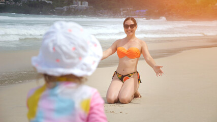 Happy mother and daughter running and embracing on sandy beach