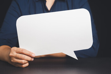 Close-up shot of a hand holding a white paper speech bubble.
