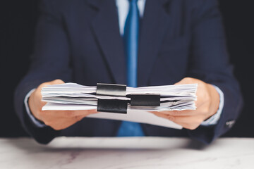 Close-up of businessman handing over a stack of paper files for approval or review.