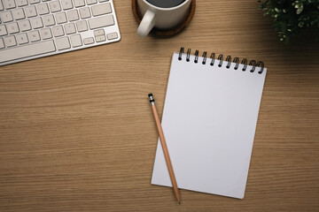 Top view of wooden desk with blank spiral notebook, keyboard and a cup coffee