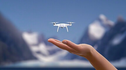 Tiny drone hovering above an outstretched hand against a snowy mountain backdrop