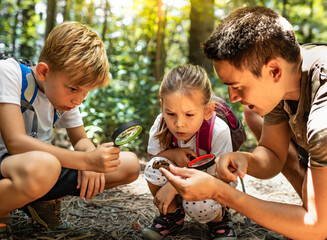 parent and children hiking exploring forest with magnifying glass learning about nature	
