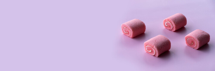Four pink cupcakes resembling rolled pastries are arranged on a soft rose-patterned surface.